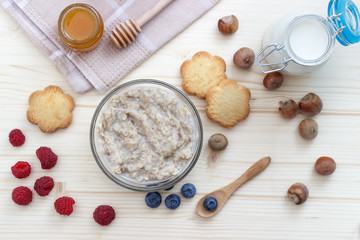 Breakfast of oatmeal with blueberries, raspberries, cookies, honey, milk and hazelnuts