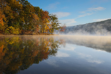 Naklejka na ściany i meble autumn sunrise over foggy lake with colorful foliage reflection with blue sky