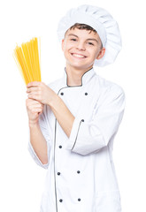 Cheerful handsome teen boy wearing chef uniform. Portrait of a happy cute male child cook with raw spaghetti, isolated on white background. Food and cooking concept.