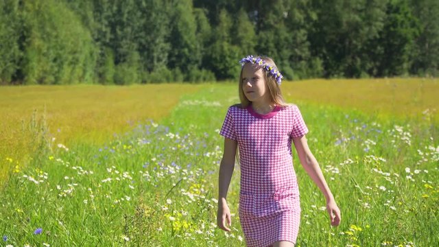 Girl walks the field, among flowers and grass. Young girl going away in green field. 4k