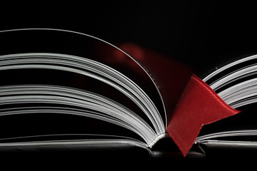 A black and white image of open book. Close-up image of  double-page spread with red bookmark on black background. Concept of gaining knowledge, learning, typography, passion for reading