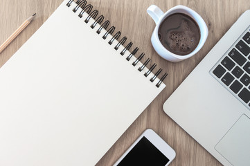Image of blank notebook paper space, cellular phone, laptop computer and coffe neatly arranged on wooden table
