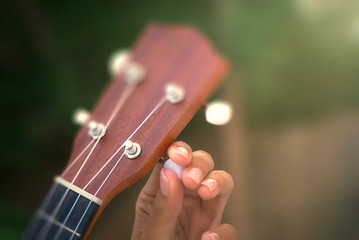 Girl tuning ukulele. Soft light and blurred image. Music instrument