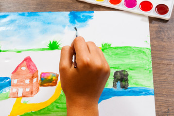 The child's hand draws a picture with watercolors. top view