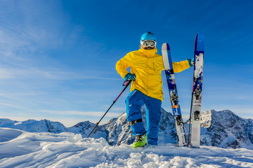 Mountaineer backcountry ski walking up along a snowy ridge with skis in the backpack. In background blue sky and shiny sun and Zebru, Ortler in South Tirol, Italy.  Adventure winter extreme sport.