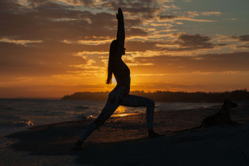 young woman practicing yoga warrior and hero pose at sunset, sunrise . Zen wellness and wellbeing concept.