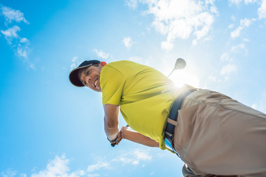 Low-angle view of a professional player wearing golf outfits while holding the club ready for the strike during individual game outdoors against cloudy sky