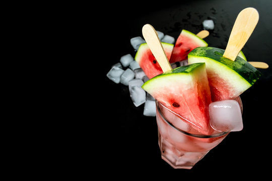 watermelon cut slice on a stick from ice cream in a glass with ice close-up on a black background