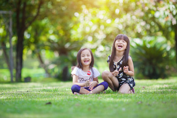 Fototapeta premium Two little girls relaxing play in the park and eat lollipops