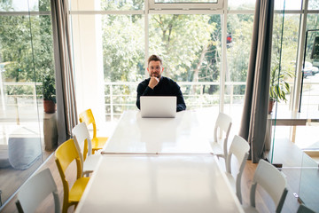 Handsome young bearded business man with laptop alone in big bright conference room
