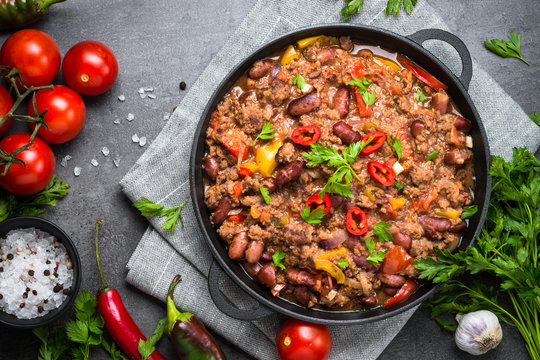 Chili con carne in iron pan on black background. Traditional mexican food.