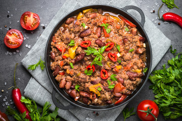 Chili con carne in iron pan on black background. Traditional mexican food.