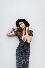 beautiful girl in a black hat and black dress with stars on a white wall background.