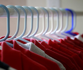 Red and one gray school uniform shirts on hangers. Selective focus.