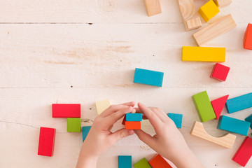 Top view on child's hands playing with colorful wooden bricks on the white table background.. Kid...