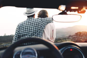 Young couple in love enjoy view and relax sitting on hood of cabriolet
