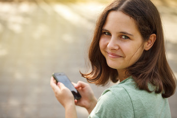 Beautiful teen girl with phone in hands. Looking at the camera, close-up.