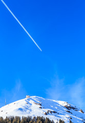 Airplane in a blue sky with traces. Mountain Hohe Salve  in winter. Ski resort Brixen im Thalef, Tyrol, Austria