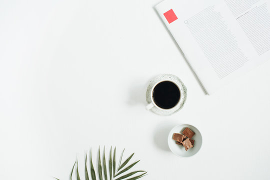 Morning Breakfast With Coffee Cup And Chocolate With Tropical Palm Leaf And Magazine On White Background. Flat Lay, Top View Women Background.