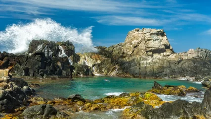 Foto auf Acrylglas Karibik Spektakuläre Welle spritzt gegen die Felsen, die den natürlichen Pool (Conchi), eine beliebte Touristenattraktion, auf Aruba abschirmen.