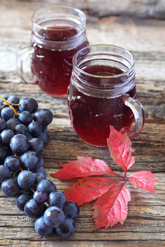 Glasses of grape juice, black grapes and autumn leaves