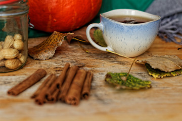 Cup of tea, cinnamon sticks, pumpkin and autumn leaves on a wooden table
