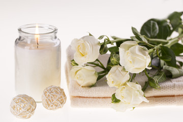 Fototapeta na wymiar Spa. Burning candle, white roses and a towel on a white background