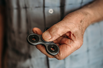 The hand of an elderly man holds Fidget Spinner