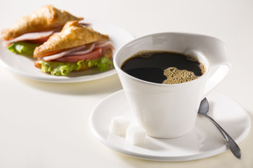 Coffee in a white cup with sandwiches. Breakfast is light.