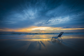 relaxing morning beach chair dramatic early sunrise color sky ocean surf water reflection scene solitude luxury resort vacation