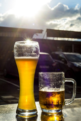 Two beer mugs stand on a granite table on the background of cars. Drink beer before driving a car