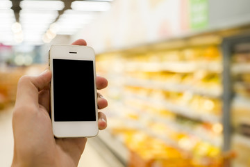 Man hand holding mobile smart phone on Supermarket blur background, business concept
