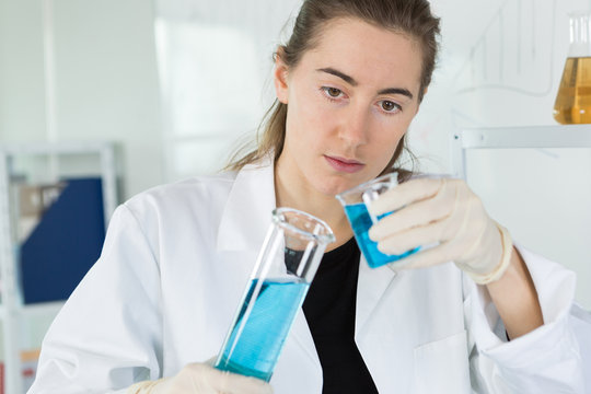 female scientist putting blue liquid into the flask