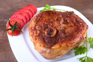 grilled pork chop with sliced tomato and sauce on wooden table.