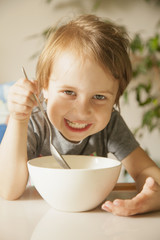 Happy cute little girl laughing and having breakfast muesli with milk at home in the kitchen (healthy food, eating, children, childhood concept )