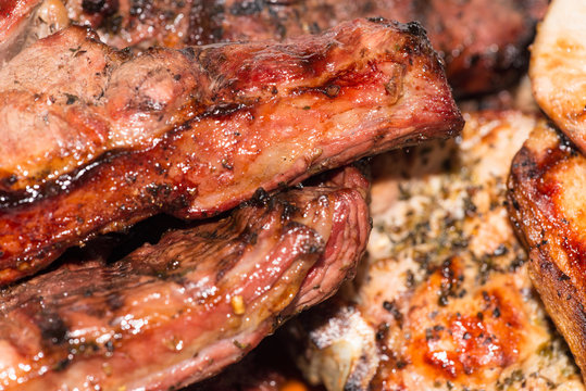 Close-up of seasoned pork chops and lamb steak cooked on charcoal BBQ grill.