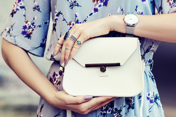 Close up photo of white leather bag in hands of fashionable woman pising in street. Model wearing...