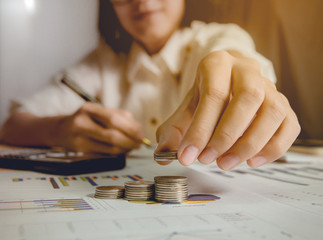 Business woman picking coins and stacking.There is right hand holding a pen in background. Shallow depth of field. Focus at finger tip.
