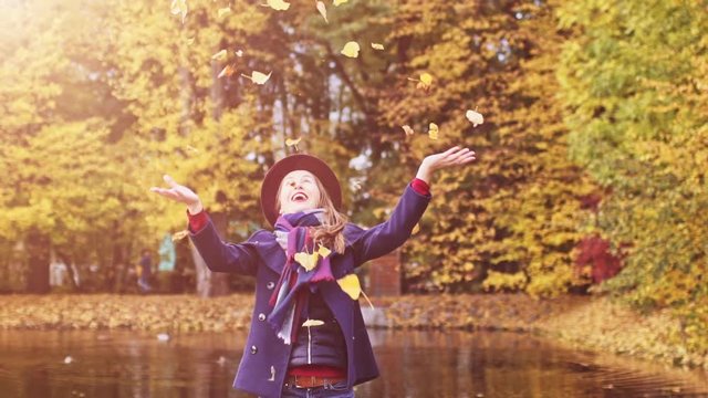 Happy Young Woman throwing leaves in Autumn Park. SLOW MOTION 120 FPS. Joyful and excited girl having fun enjoying sunny fall outdoors. 