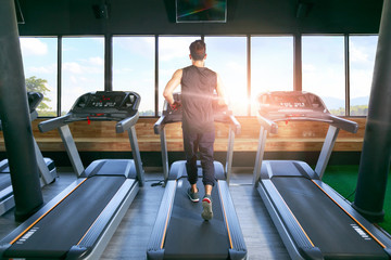 Back view of young man athlete with running on treadmill in gym.