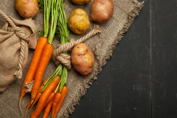 Raw potatoes and carrots on a black wooden background