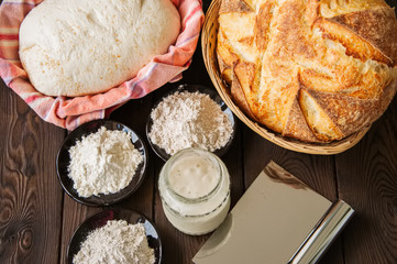 Homemade bread dough, sourdough in a jar, mix of flours, bread in basket for proof and spatula on a wooden background. Baking concept.