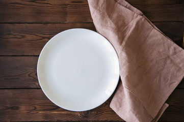 White round plate and linen napkin on a wooden background.