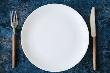 White plate and cutlery  on a blue stone background.