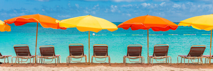 Beach chairs and umbrellas vacation tropical Holiday travel Banner. Caribbean beach on Sint Maarten with retro colorful parasols and loungers, turquoise blue ocean water. Panoramic crop.