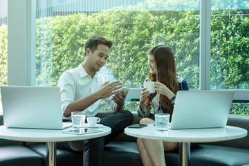 Happy Asian Beautiful young business woman and handsome businessman with formal suits are talking and using a laptop and smart phone for meeting in modern office, business people concept