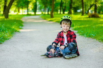 Boy in a protective helmet and protective pads for roller skating sitting on the road