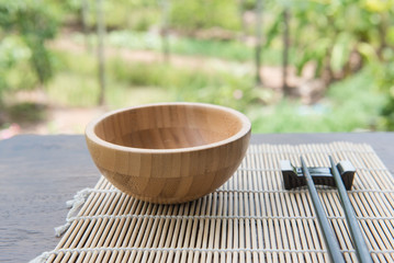 Wooden bowl with chopsticks on bamboo mat  on wooden table in the garden.