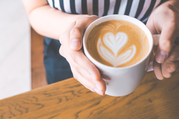 Woman's hand holding a coffee latte cup art on wooden desk