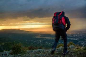 Amazing sunset on a mountain top - man with alpine equipment rushing camera right under the stormy sky